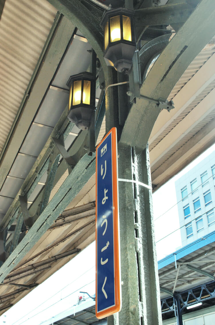 写真：「りょうごく」とひらがなで書かれた青とオレンジの駅名板